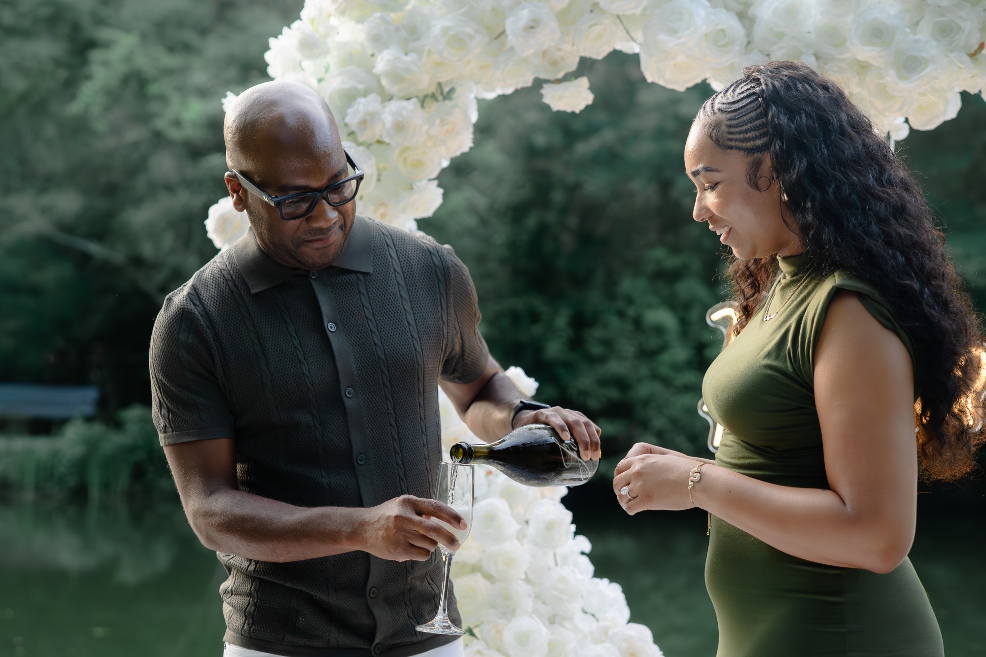 Newly engaged couple pouring champagne in front of a white rose heart arch after a surprise proposal in Houston