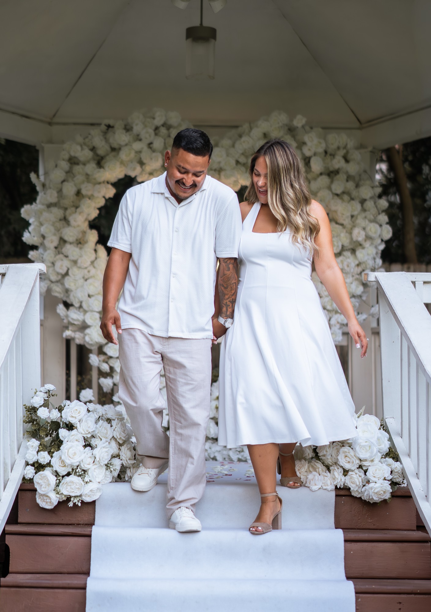 Couple walking down gazebo steps lined with white roses after a custom proposal setup